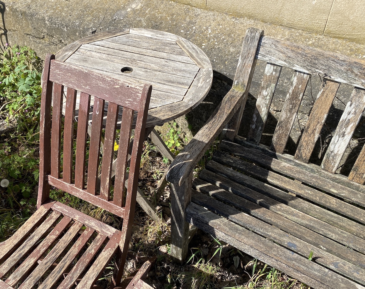 A weathered teak garden bench, width 148cm, height 88cm, a circular folding table and three folding chairs